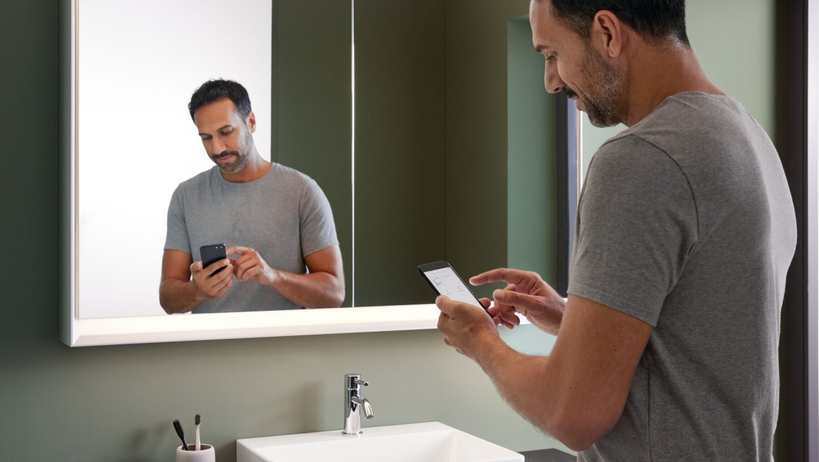 Чоловік стоїть у ванній кімнаті з мобільним телефоном
