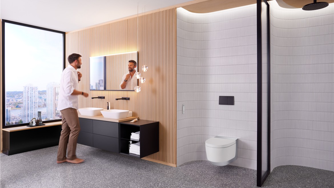 Чоловік у ванній кімнаті стоїть перед дзеркалом Geberit Option Plus Square і чорними меблями Geberit ONE