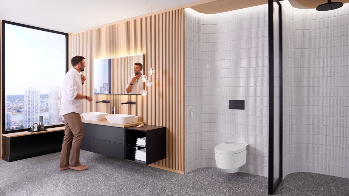 Чоловік у ванній кімнаті стоїть перед дзеркалом Geberit Option Plus Square і чорними меблями Geberit ONE Чоловік у ванній кімнаті стоїть перед дзеркалом Geberit Option Plus Square і чорними меблями Geberit ONE