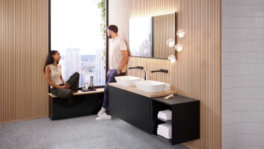Жінка та чоловік у великій ванній кімнаті з накладними умивальниками Geberit ONE, дзеркалом Option і дерев’яними деталями