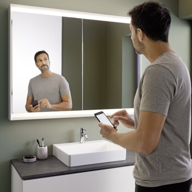 Чоловік керує освітленням дзеркальної шафи Geberit ONE за допомогою смартфона